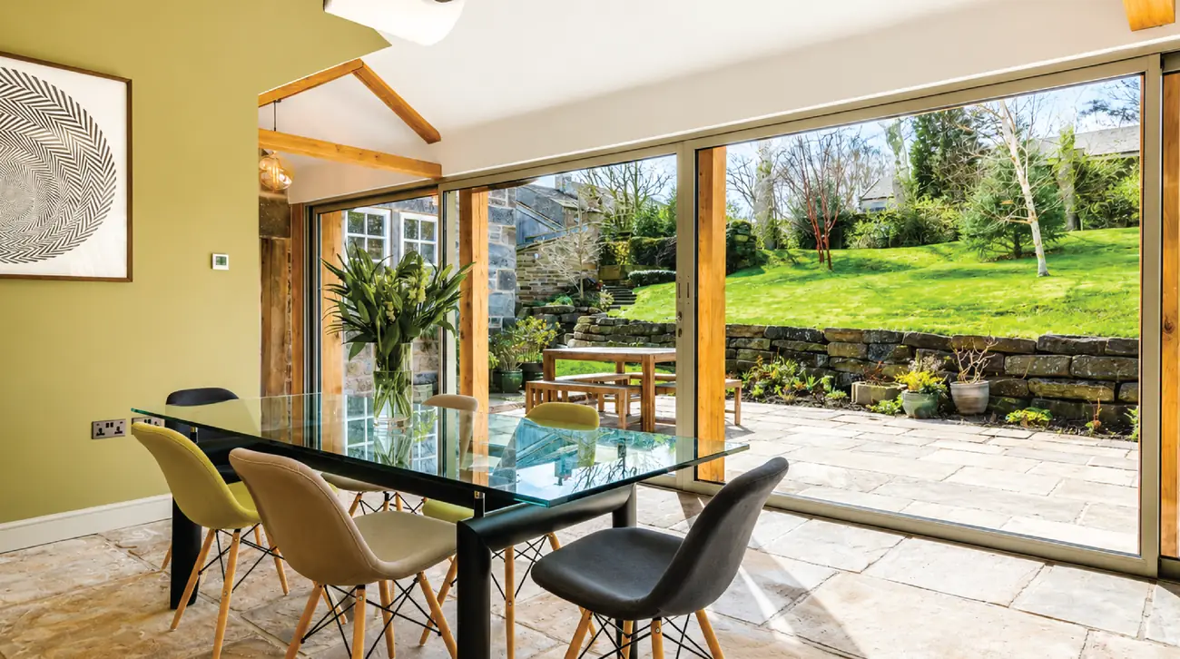 Dining area with a glass table and wide sliding doors framing the garden and dry stone wall
