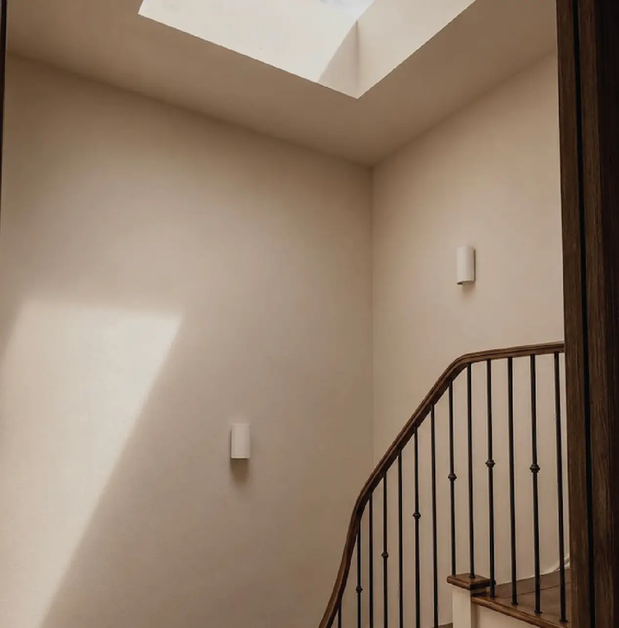 Sweeping timber staircase with slender wrought-iron spindles beneath a rooflight