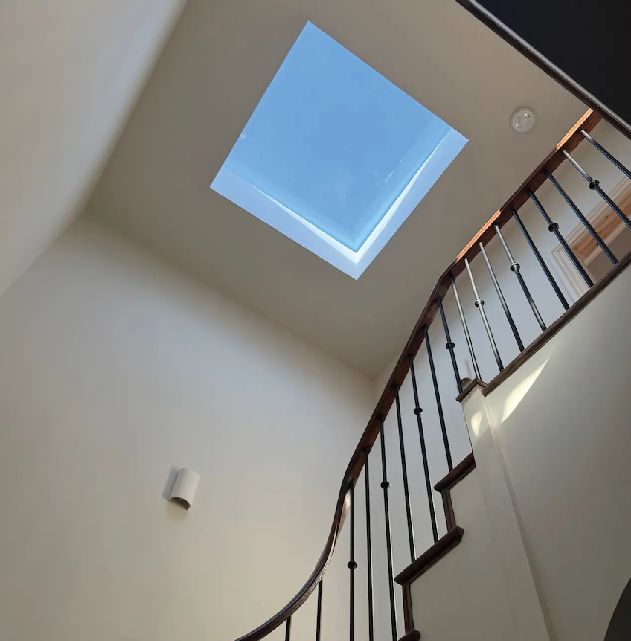 Curved staircase rising beneath a rooflight to the top floor