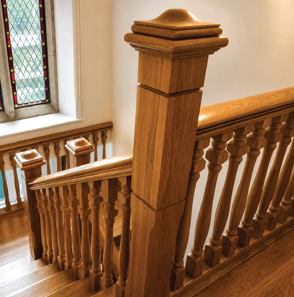 Turned oak spindles and a moulded newel post beside a leaded stained-glass window