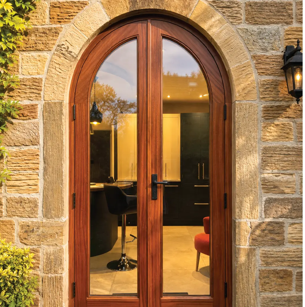 Arched hardwood French doors in a stone opening, lit from within